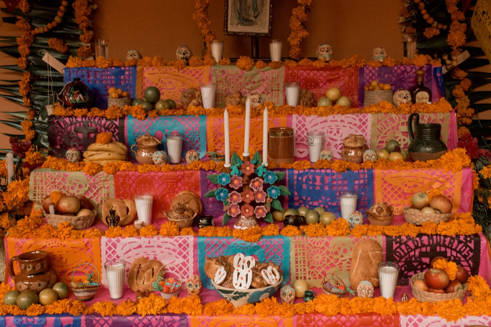 Ofrenda de Día de Muertos de varios niveles, con panes, veladoras, papel picado y cempasúchil