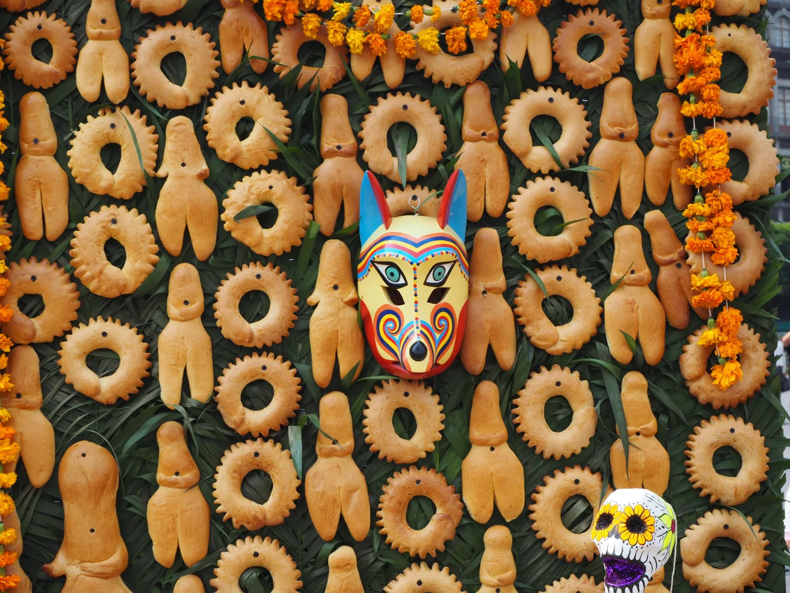Panes de muerto con forma de persona y roscas, colgados en una ofrenda de la Ciudad de México con cempasúchil