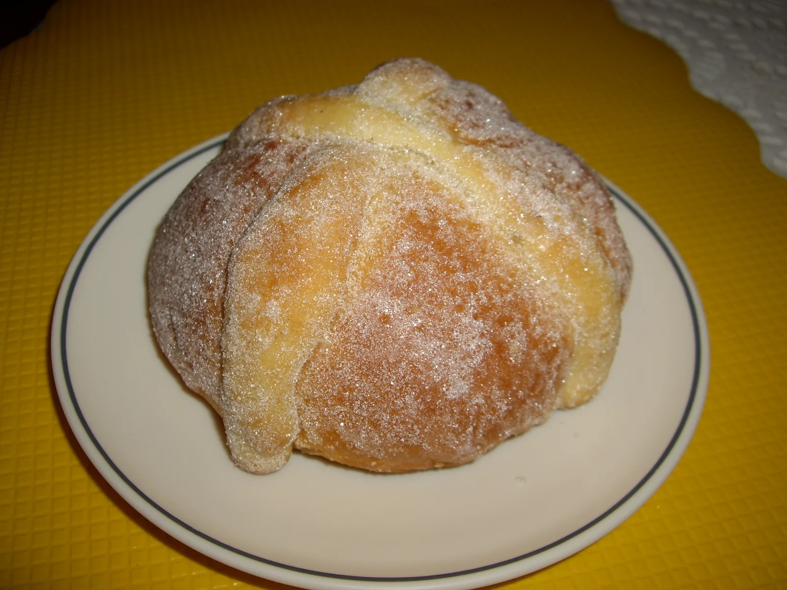 Pan de muerto espolvoreado de azúcar en un plato, con sus canillas cruzadas encima